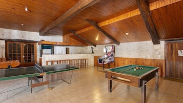 A billiards room with a pool table, a foosball table, and a bar area.