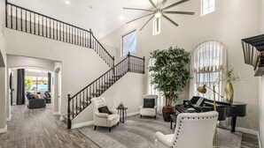 Un vaste espace de vie agrémenté d’un magnifique escalier, d’un piano et de sièges confortables.
