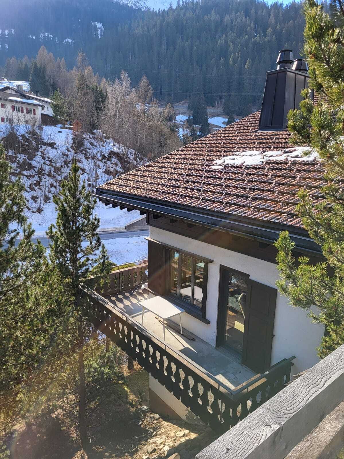 Una casa moderna con tetto in tegole, un balcone con ringhiera e vista su un paesaggio innevato.