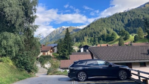En sort bil parkeret i et landligt område med huse og bjerge i baggrunden.