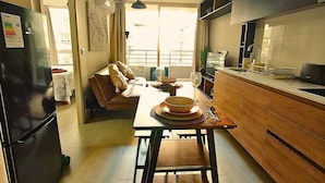 A modern kitchen with wooden cabinets, a dining table set for four, and a large window providing natural light. - Rosas Confort 409 (Santiago)