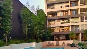 A swimming pool with a wooden deck, surrounded by a building with balconies and a garden area. - Rosas Confort 409 (Santiago)
