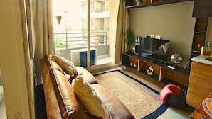 A living room with a sofa, TV, and a view of a balcony. - Rosas Confort 409 (Santiago)