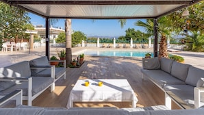 Un espace extérieur aménagé, abrit é et doté d’une piscine, de mobilier blanc et offrant une vue sur la mer.