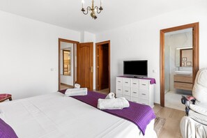 A hotel room with a bed, a television, a bathroom mirror, and a door leading to another room.