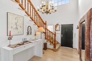 A staircase with wooden balusters, a chandelier, and artwork on the walls.