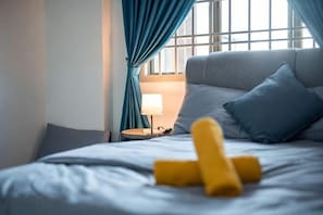 A bed with a blue headboard, a lamp on a bedside table, and a window with curtains.
