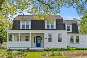 A two-story house with a front porch, a blue door, and a small garden area.