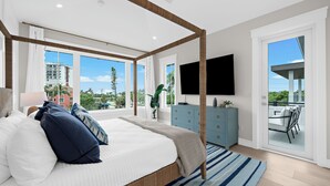 A modern bedroom with a large bed, a TV, a balcony, and a view of the city.