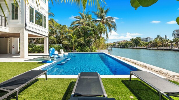 A modern house with a swimming pool, lounge chairs, and a view of the water.