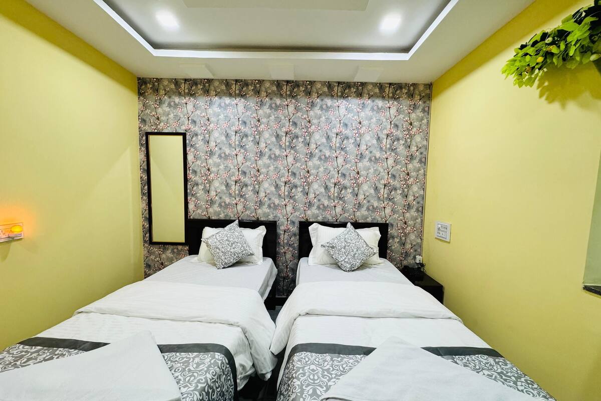 Une chambre double avec deux lits, une tête de lit recouverte d’un papier peint à motifs floraux, une table de chevet avec une lampe et un miroir au mur.