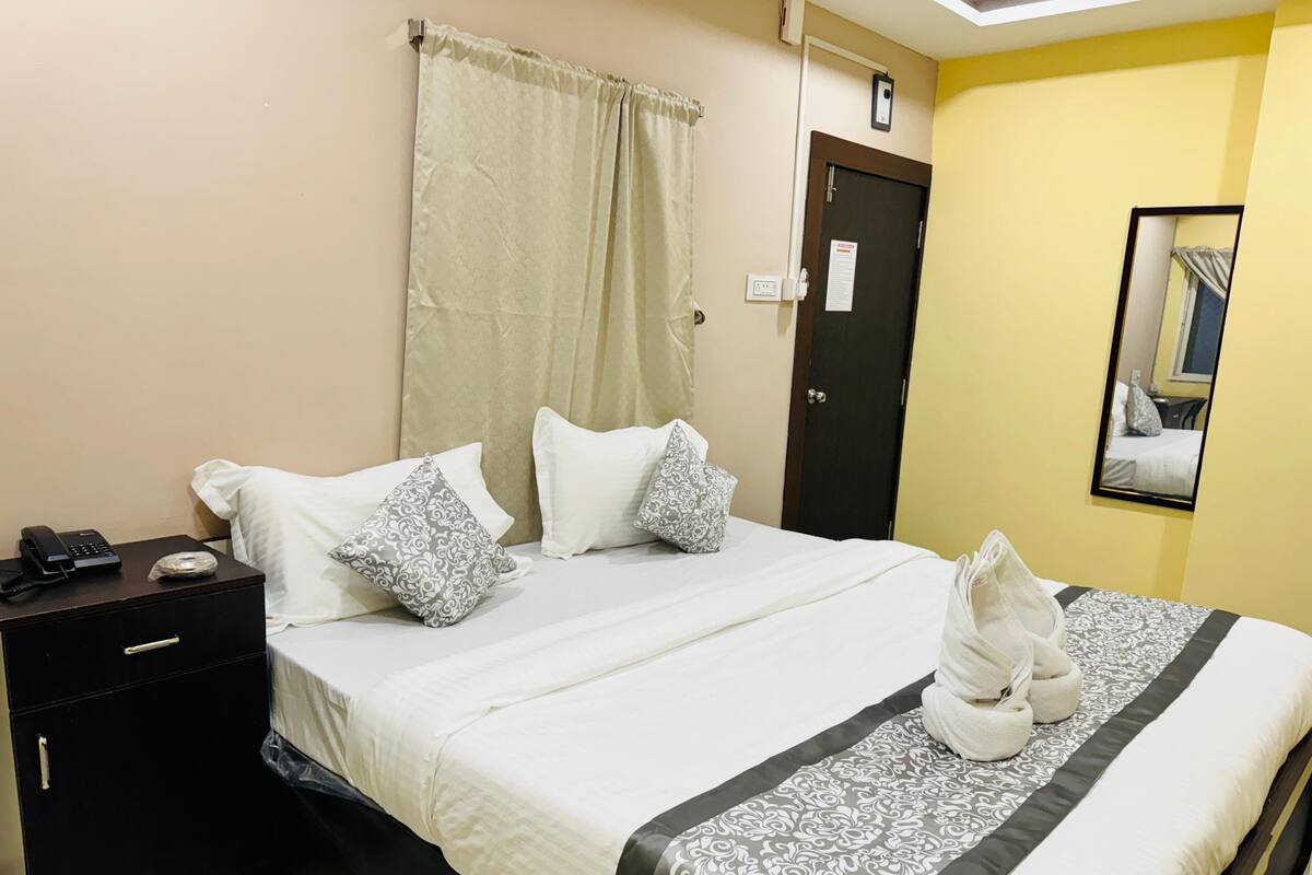 Une chambre d’hôtel avec un lit, une table de chevet, un téléphone, un miroir et une porte.