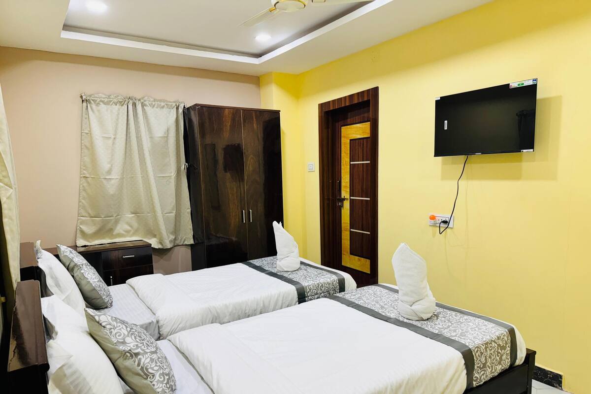 Une chambre d’hôtel avec deux lits, une armoire, un téléviseur fixé au mur et un ventilateur de plafond.