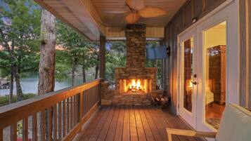 Une terrasse en bois avec une cheminée en pierre, un ventilateur de plafond et une vue sur un lac.