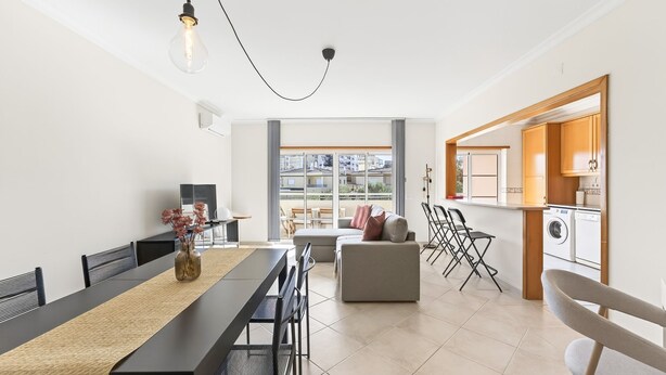 A modern apartment with a dining area, sofa, kitchen, and a view of the city.