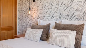 A bedroom with a bed, pillows, a nightstand, a wall with a floral pattern, and a hanging light fixture.