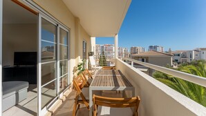 A balcony with a wooden table and chairs, a TV, and a sliding glass door.