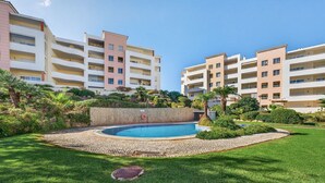 A multi-story hotel with a swimming pool surrounded by well-maintained lawns and palm trees.