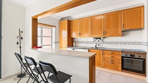 A kitchen with wooden cabinets, a granite countertop, and a built-in oven. There are three black chairs and a small island with a sink.