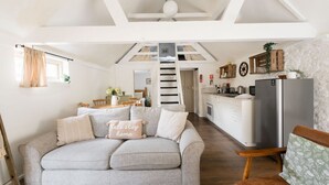 Amplia sala de estar con sofá, cocina y escalera que lleva a un nivel superior.