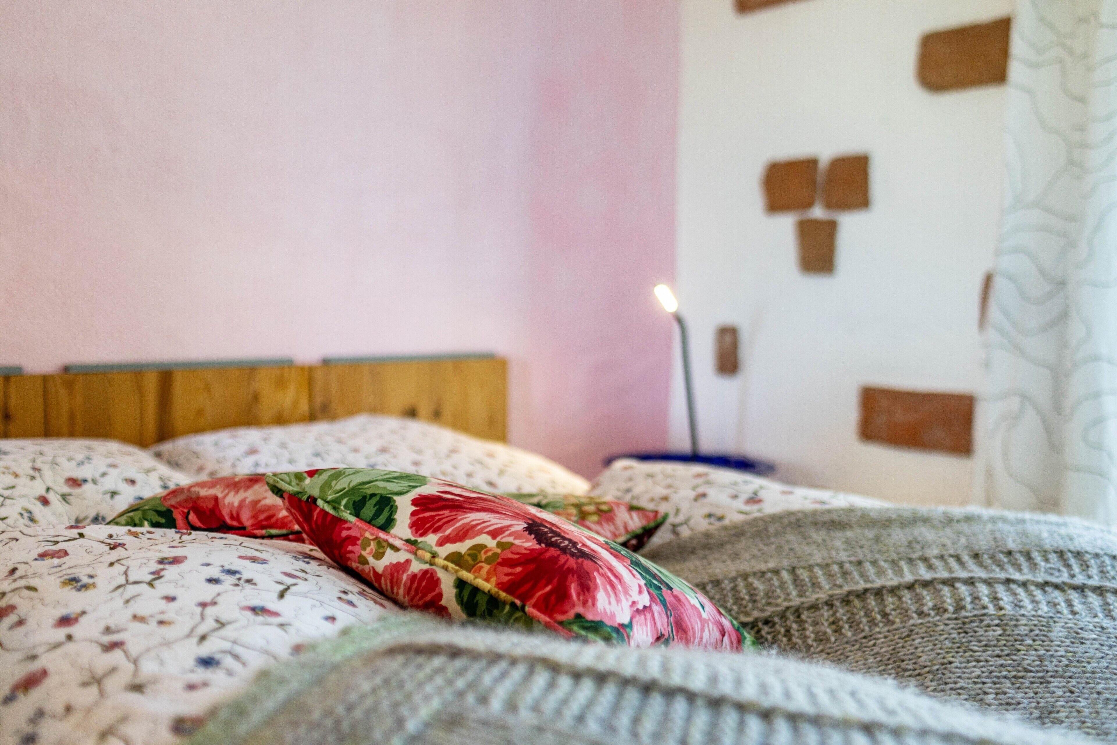 Een bed met bloemenbeddengoed, een houten hoofdbord en een muur met een lichtschakelaar en stopcontact.