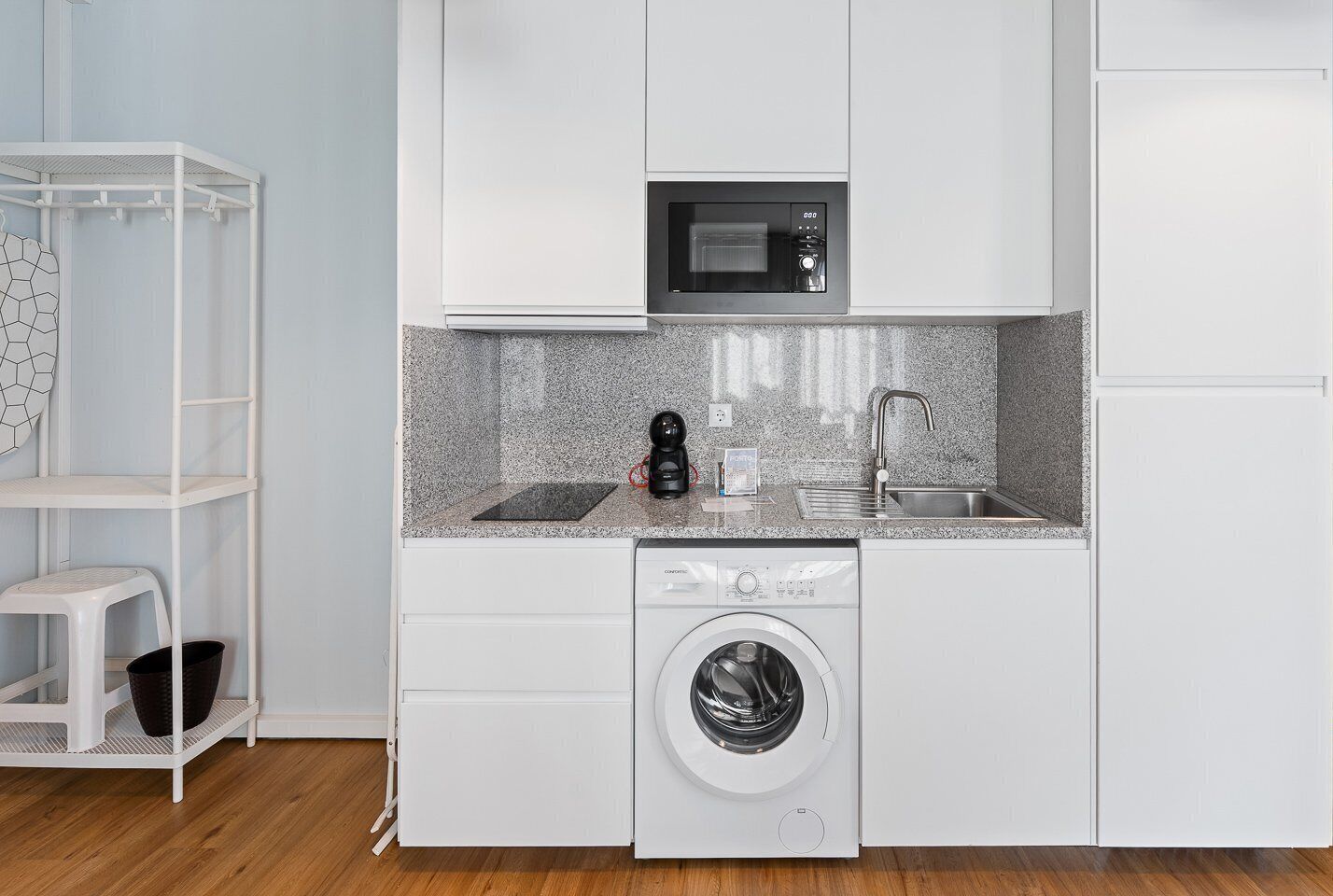 Een kleine keuken met een magnetron, spoelbak en een ingebouwde wasmachine.