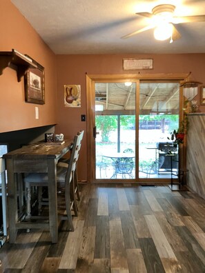 A dining area with a wooden table and chairs, a ceiling fan, and a view through a glass door to an outdoor patio.