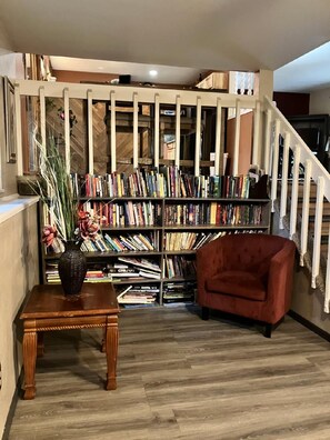 Une pièce avec un plancher en bois, un fauteuil rouge, une bibliothèque remplie de livres et un escalier avec des rampes blanches.