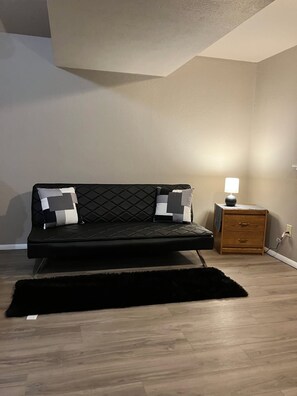 Une chambre moderne avec un canapé noir, une table de chevet en bois et un tapis noir.