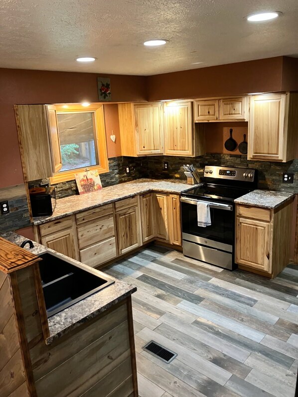 A kitchen with wooden cabinets, a granite countertop, a stainless steel oven, and a stone backsplash.