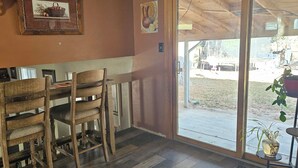 Een eethoek met houten stoelen en een tafel, een houten plafond en uitzicht op het landschap door een glazen deur.