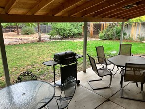 Une terrasse extérieure avec un barbecue, des chaises en métal et une table en verre.