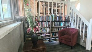 Een trap met een witte leuning die uitkomt op een plateau. Daaronder is een boekenplank vol boeken en een rode fauteuil te zien.