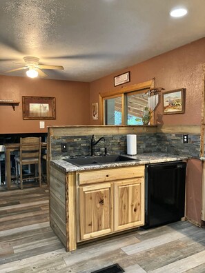 Une cuisine avec des meubles en bois, un plan de travail en granit, un lave-vaisselle noir et un ventilateur de plafond.
