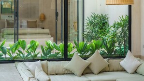 Un salon moderne avec un grand canapé d’angle, une table basse en bois et une porte vitrée donnant sur un balcon agrémenté de plantes.