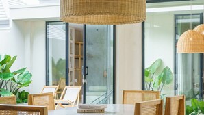 Un espace repas moderne avec une table ronde, des chaises en bois et un grand luminaire suspendu en fibres tressées.
