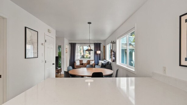 A modern kitchen with a large island, a dining area with a round table, and a view of the outdoors through large windows.