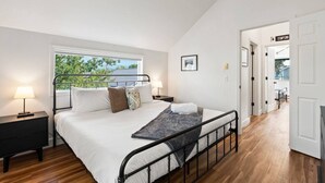 A bedroom with a bed, bedside tables, a window with a view, and a door leading to another room.
