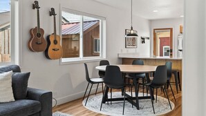 A modern kitchen with a dining area, featuring a round table, black chairs, and a hanging light fixture.