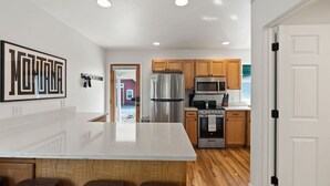 A modern kitchen with white countertops, wooden cabinets, stainless steel appliances, and a large island with bar stools.