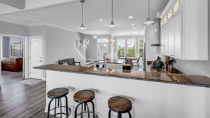 Una cocina amplia con una isla grande, taburetes de bar, iluminación colgante y vistas al área de comedor.