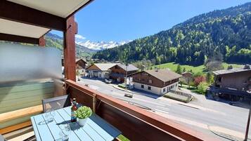 A balcony with a table and chairs, overlooking a street with buildings and a mountain range.