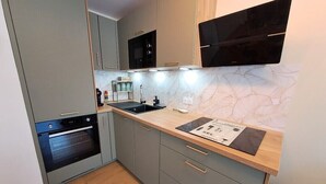 Une cuisine moderne avec des armoires grises, un four encastré, un plan de travail en bois et un revêtement mural à motifs géométriques.
