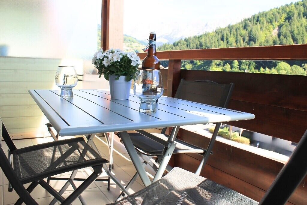 A balcony with a table, chairs, a bottle, and a flower arrangement.