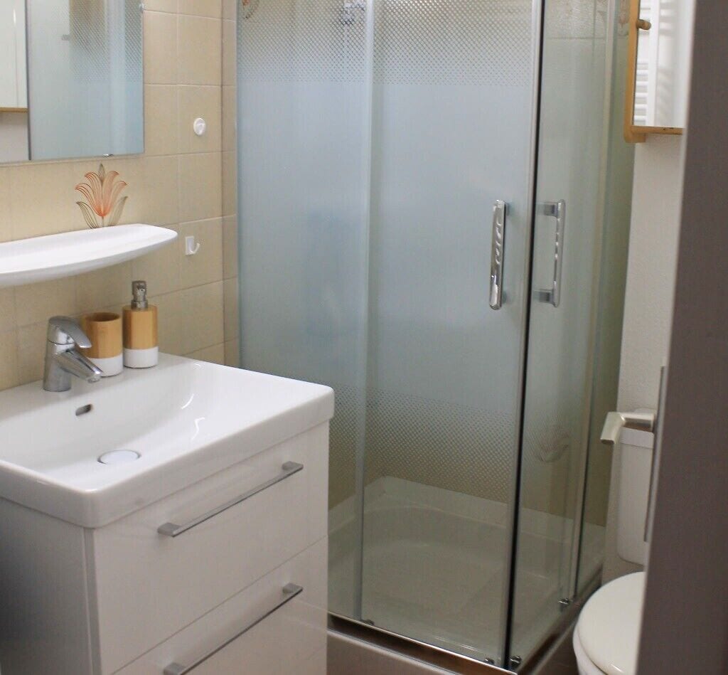 Ein Badezimmer mit Waschbecken, Spiegel und Duschkabine aus Glas.
