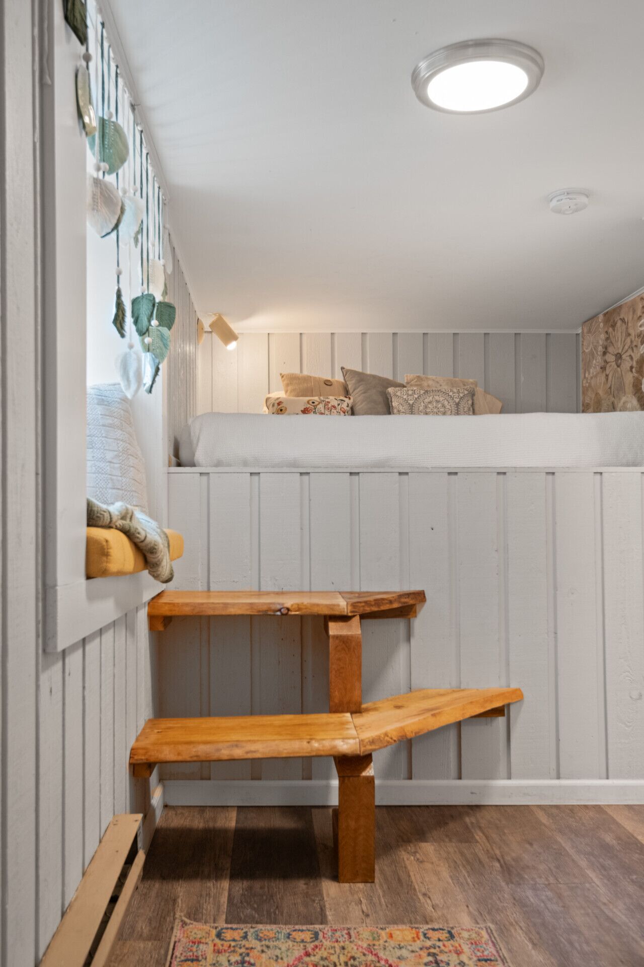 A cozy room with a bunk bed, a wooden bench, and a patterned rug.