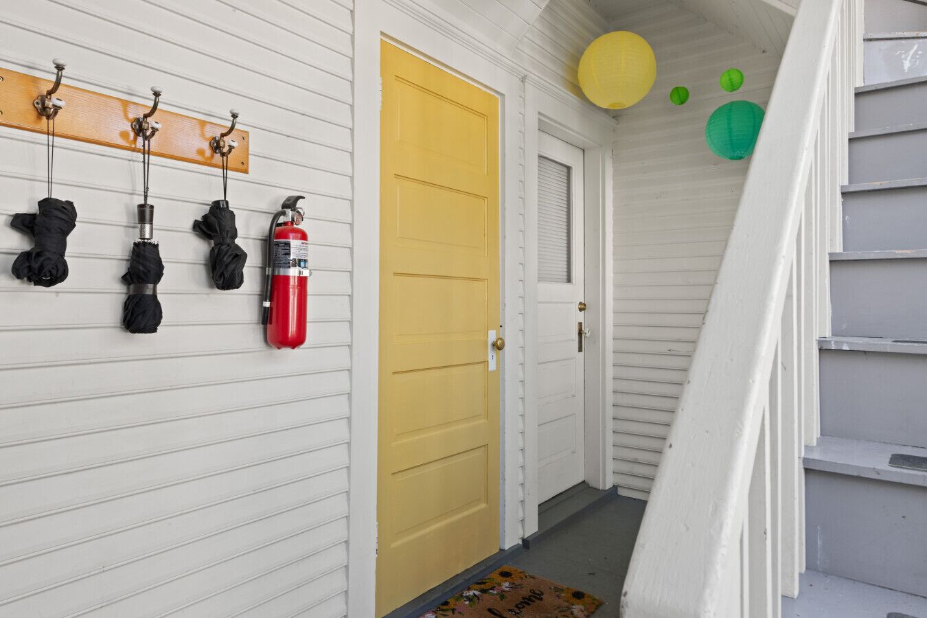 A hallway with a yellow door, a fire extinguisher, and black umbrellas hanging on hooks.