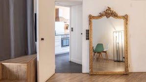 Ein Zimmer mit einem großen, verzierten Spiegel, einer hölzernen Bank und Blick in einen Küchenbereich.