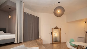 Ein modernes Hotelzimmer mit einem Bett, einer Couch, einem Esstisch mit Stühlen, einem Spiegel und einer Pendelleuchte.