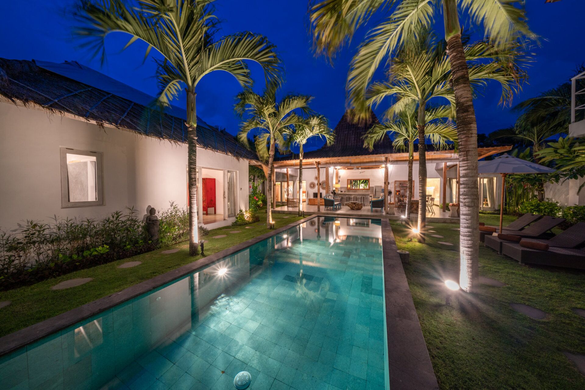 A swimming pool surrounded by palm trees and a building with a thatched roof.